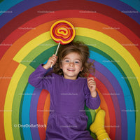 Smiling child lying on vibrant rainbow floor with lollipop