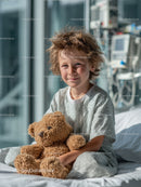 Child Sitting Comfortably in Hospital Bed Holding Teddy Bear