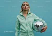 Young Woman in Mint Green Tracksuit Holding Disco Ball in Studio