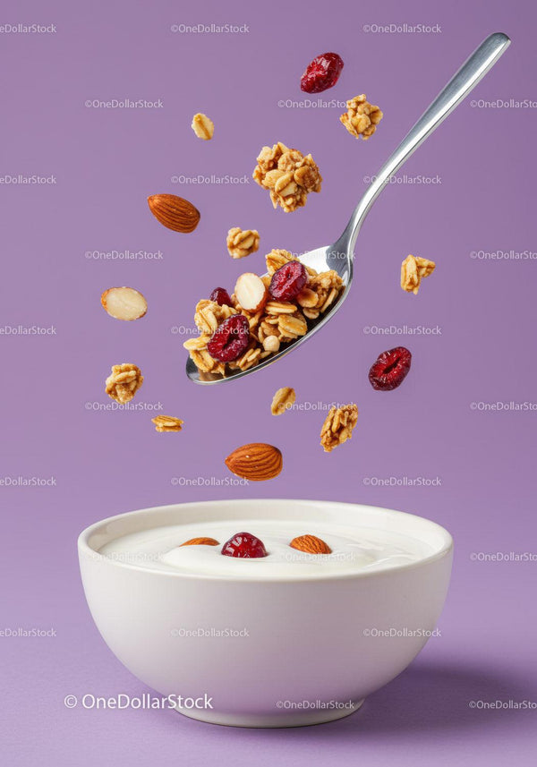 Granola, orzechy i jagody spadające do kremowej miski jogurtu
