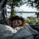 Peaceful outdoor scene of a woman sleeping by a lakeside beneath lush green trees