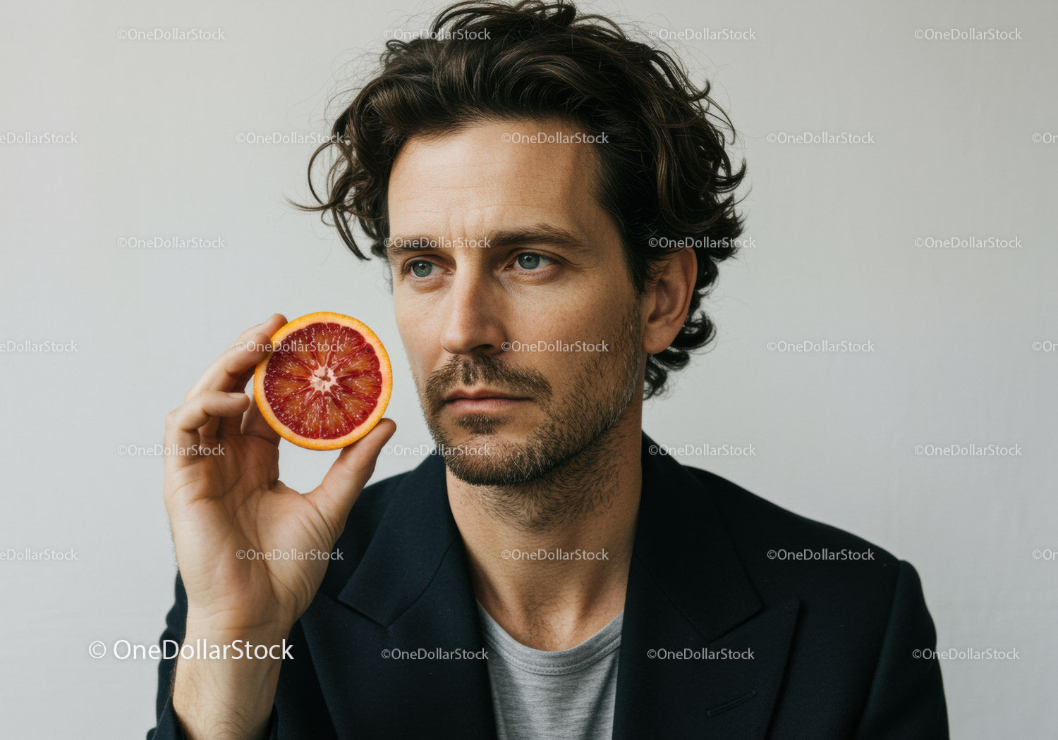 Man Holding Blood Orange Slice with Thoughtful Expression