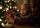Adult and toddler holding gift by Christmas tree lights