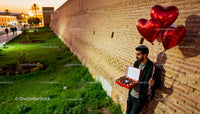 Man holding chocolates and heart balloons by brick wall