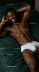 Smiling young man relaxing on dark green bed sheets