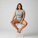 Confident Young Woman Sitting on Stool in Casual Grey Outfit