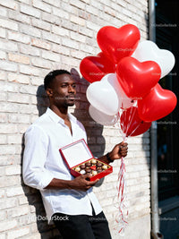Man holding heart balloons and chocolates near brick wall