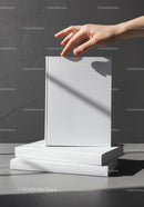 Hand Reaching for a Blank White Book on Stack