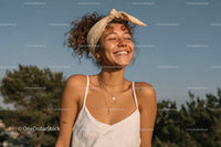 Joyful Young Woman with Curly Hair and Headband in Sunlit Outdoors