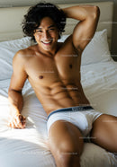 Smiling athletic man relaxing on bed in white underwear