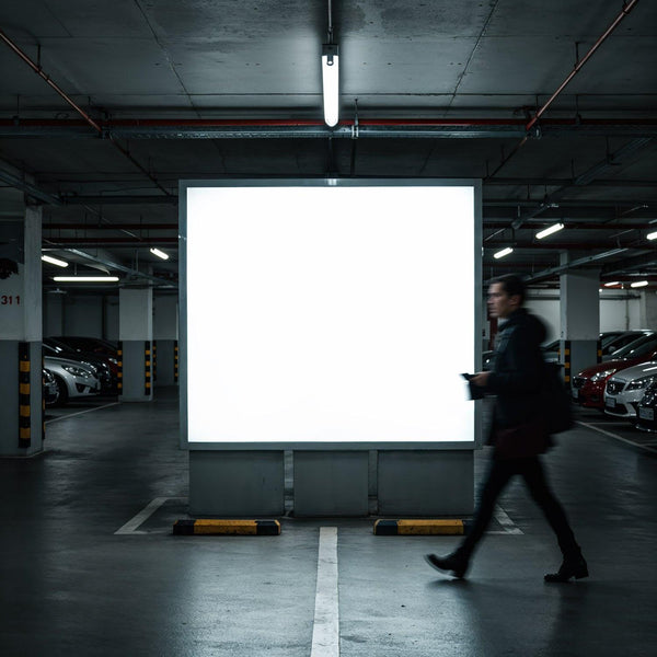 Man walking past illuminated billboard in parking garage JPG Mockup Image