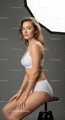 Elegant Young Woman in White Fitness Wear Sitting on Bar Stool in Studio