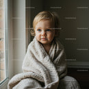 Toddler wrapped in cozy blanket by window light