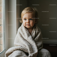 Toddler wrapped in cozy blanket by window light