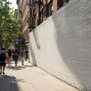City sidewalk with white brick wall and pedestrians during sunny day