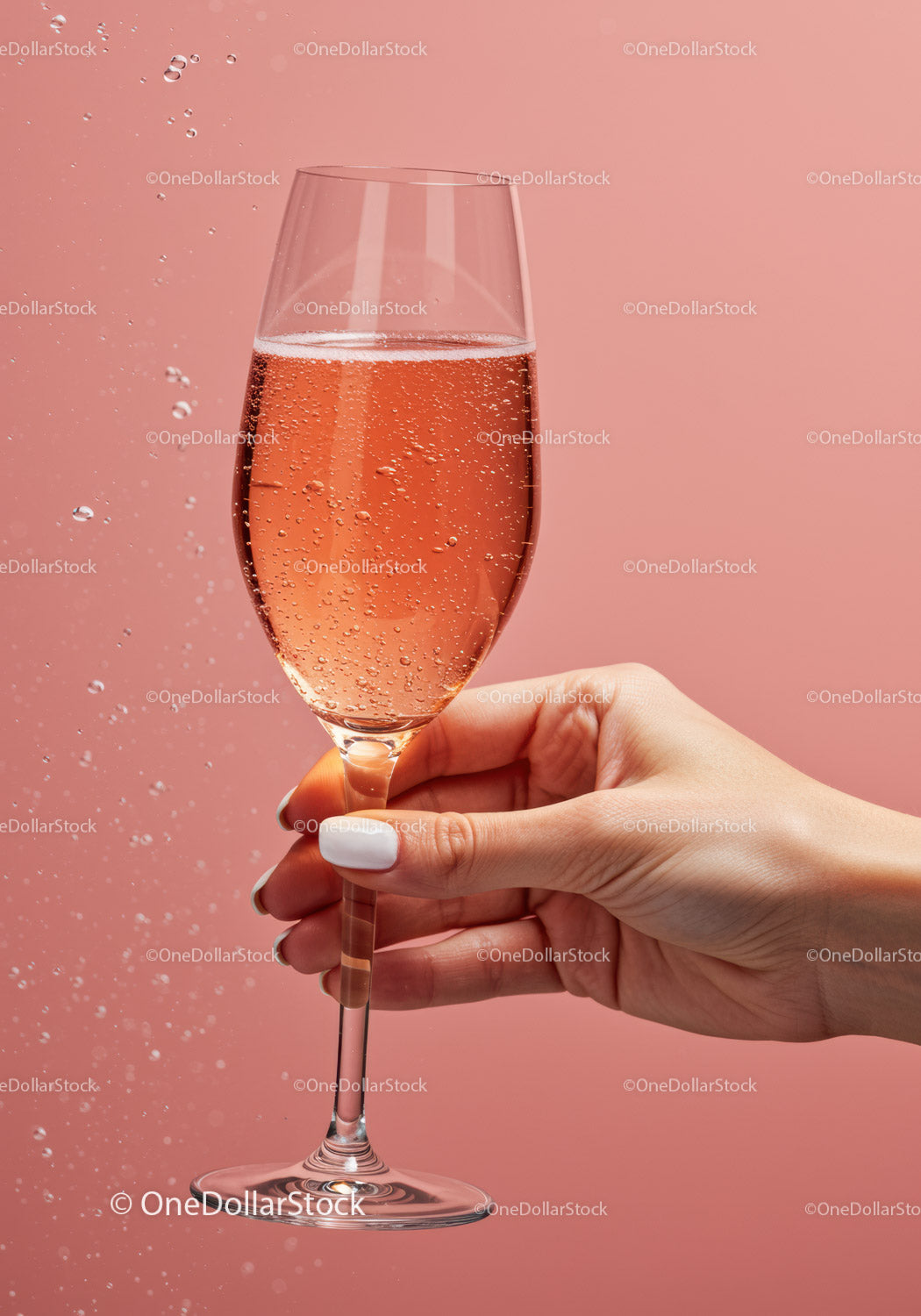 Hand holding sparkling rosé wine glass on pink background