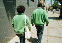 Two People Walking Side by Side in Green Sweaters on City Street