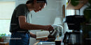 Woman pouring coffee while reading a book in kitchen