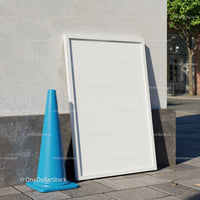 Blank white frame leaning on urban wall with traffic cone
