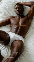 Athletic man relaxing in white briefs on bed