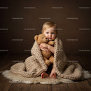 Toddler wrapped in knit blanket holding teddy bear