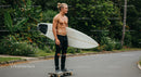 Young Man with Surfboard Skateboarding in Tropical Outdoor Setting