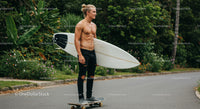 Young Man with Surfboard Skateboarding in Tropical Outdoor Setting