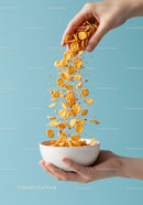 Hand Pouring Cornflakes Into White Bowl On Blue