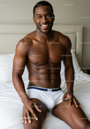 Smiling muscular man sitting on white bed in underwear