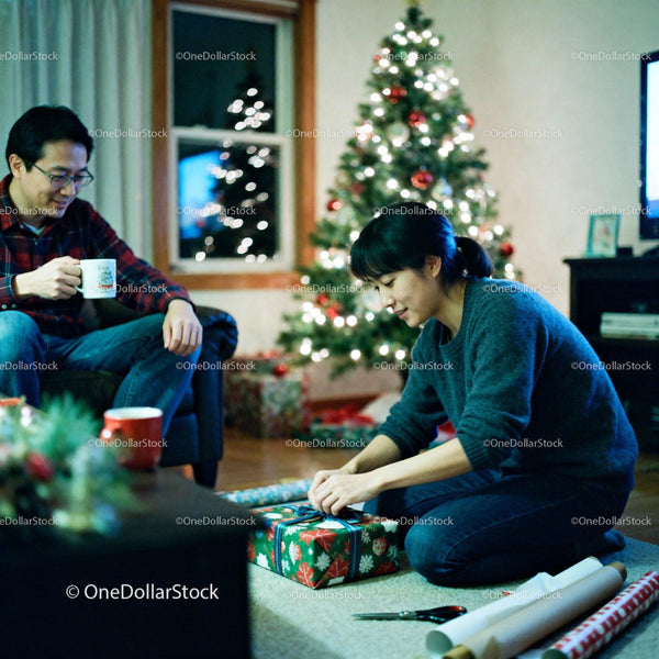 Couple wrapping Christmas gifts by decorated tree at home