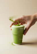 Hand Sprinkling Matcha Powder on Frothy Green Tea Latte
