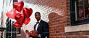 Handsome man in tuxedo holding heart balloons and chocolates