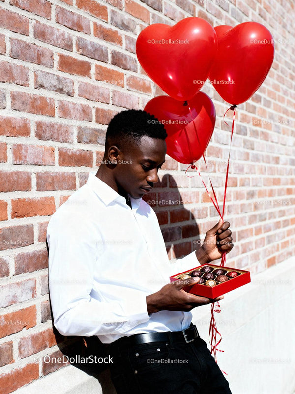 Man holding heart balloons and chocolate box outdoors