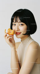 Young woman with black hair holding mandarin orange smiling portrait