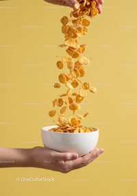 Hand Pouring Crunchy Cornflakes into White Bowl