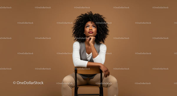 Stylish Young Woman Sitting on Chair with Curly Hair in Casual Outfit