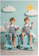 Twin boys sitting on suitcases with paper planes