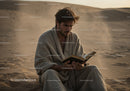Man Reading Book in Desert Surrounded by Sand Dunes