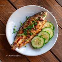 Grilled Fish with Cucumber Slices and Fresh Herbs on White Plate