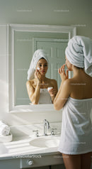 Woman Applying Face Cream in Mirror in Bright Bathroom
