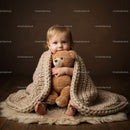Toddler wrapped in knitted blanket hugging teddy bear