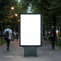 Empty illuminated billboard on city park walkway at dusk