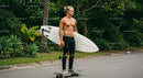 Young Man with Surfboard Skateboarding in Tropical Environment