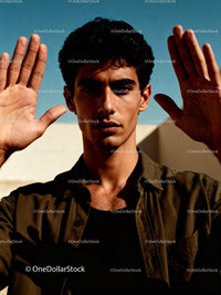 Serious young man raising hands under bright sunlight