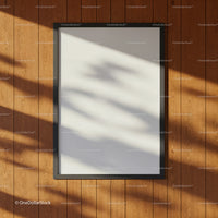 Blank black frame on wooden wall with soft shadows