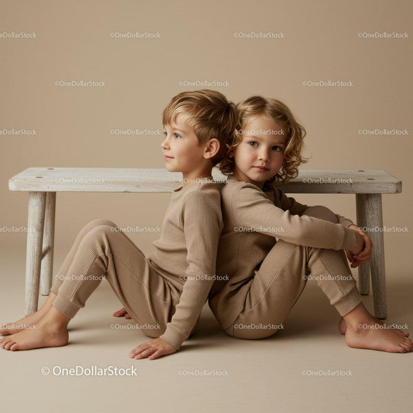Two children sitting back to back on beige floor indoors