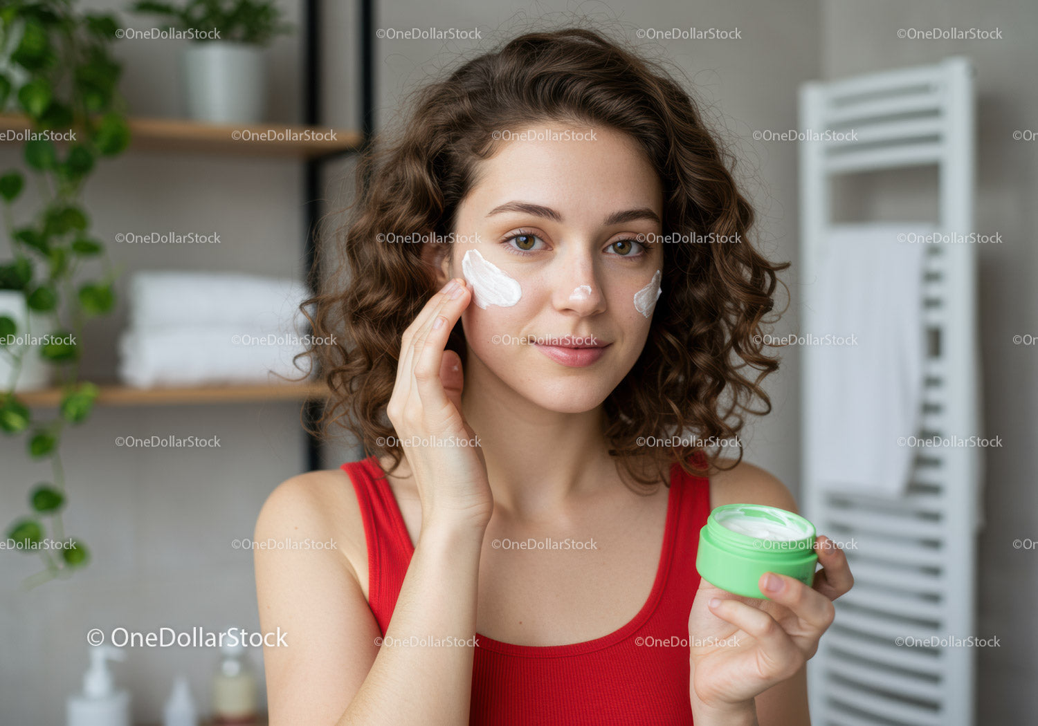 Młoda kobieta nakładająca krem do twarzy w łazience z produktami do pielęgnacji skóry