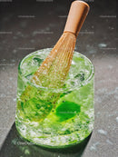 Whisk stirring vibrant green matcha in glass with ice