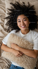 Smiling woman lying on bed hugging soft fluffy pillow