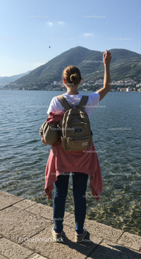 Young Woman with Backpack Taking Photo by Lake with Mountain View